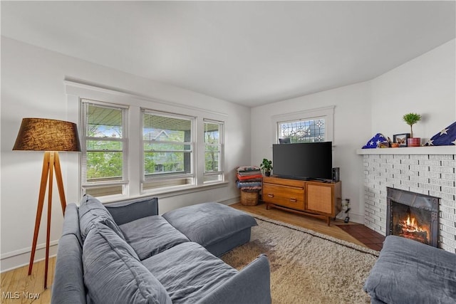 living room featuring baseboards, a brick fireplace, and wood finished floors
