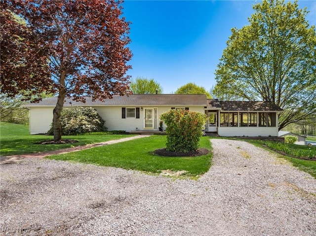 ranch-style house with a front lawn, a sunroom, and gravel driveway