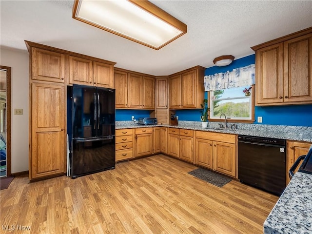 kitchen with a sink, brown cabinetry, black appliances, and light wood finished floors