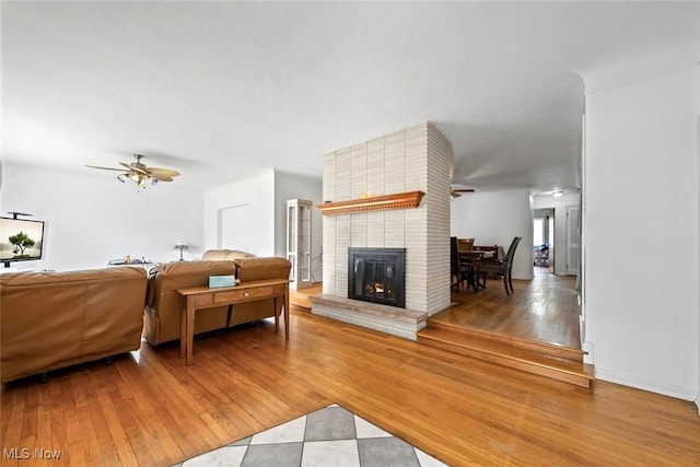 living room featuring a ceiling fan, a brick fireplace, and wood finished floors