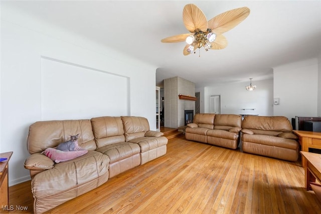 living room featuring a brick fireplace, a ceiling fan, and light wood-type flooring