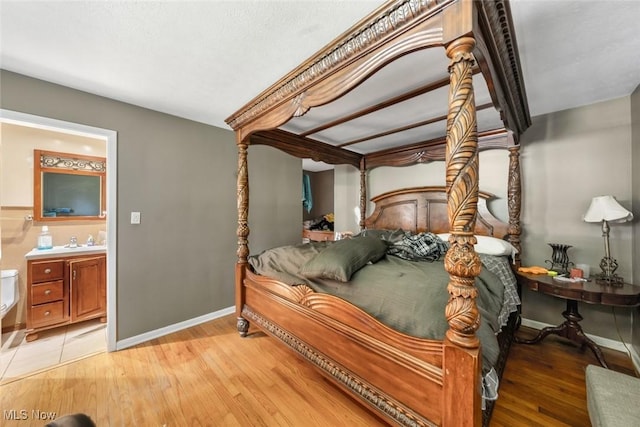 bedroom featuring baseboards, a sink, ensuite bathroom, and wood finished floors