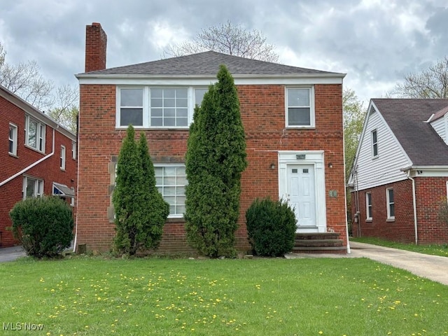 view of front of property featuring brick siding, a front yard, and a chimney