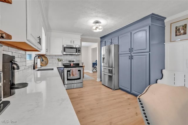 kitchen featuring appliances with stainless steel finishes, a sink, light wood-style flooring, tasteful backsplash, and ornamental molding