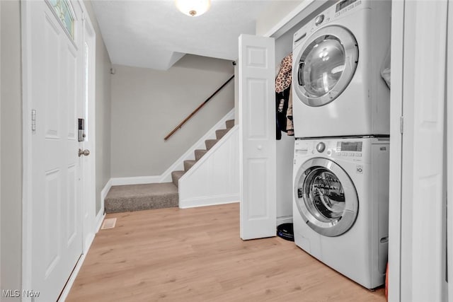washroom featuring stacked washing maching and dryer, laundry area, and light wood-style flooring