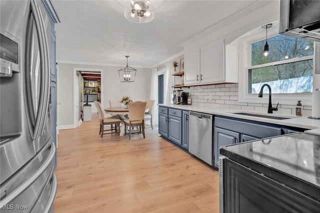 kitchen with backsplash, appliances with stainless steel finishes, a sink, a notable chandelier, and ornamental molding