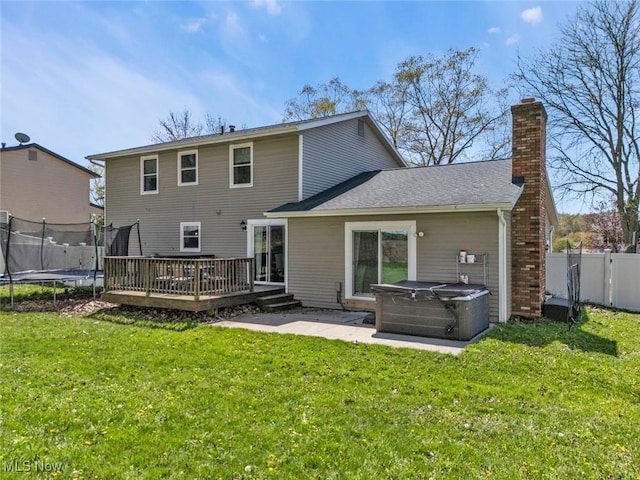 rear view of property featuring fence, a deck, a lawn, a trampoline, and a hot tub