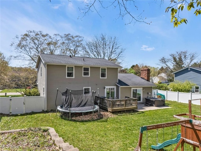 back of house with a wooden deck, a fenced backyard, a chimney, a lawn, and a hot tub