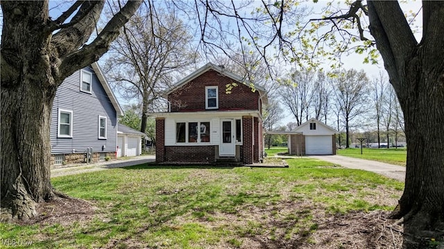 view of front of house with brick siding, a detached garage, a front yard, entry steps, and an outbuilding