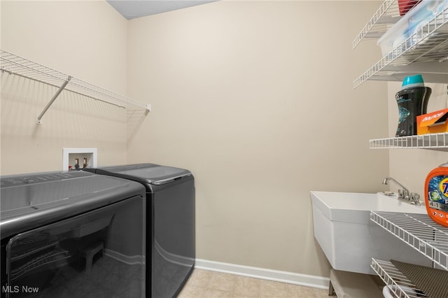 clothes washing area with independent washer and dryer, light tile patterned flooring, laundry area, a sink, and baseboards