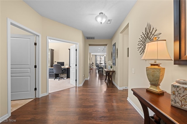 hallway with baseboards, visible vents, and wood finished floors