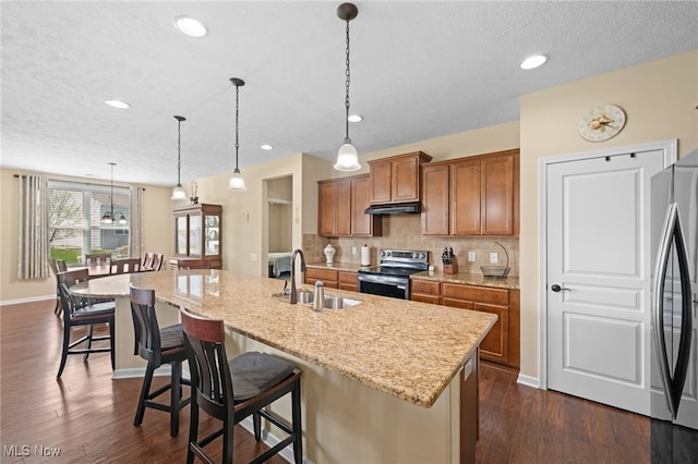kitchen featuring decorative backsplash, brown cabinetry, appliances with stainless steel finishes, a sink, and dark wood-style floors