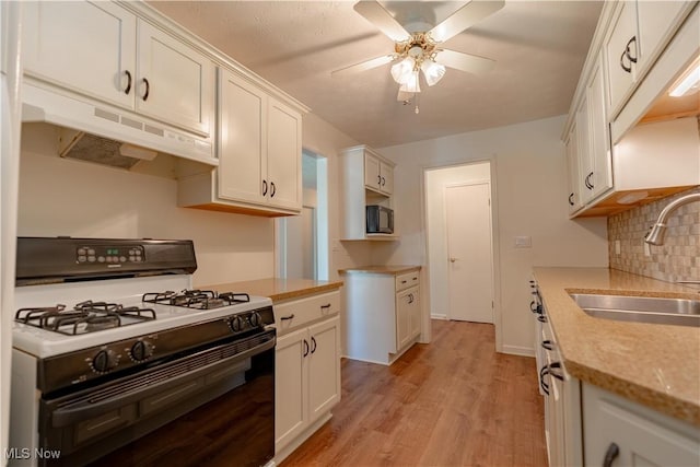 kitchen with a sink, gas range oven, under cabinet range hood, a ceiling fan, and light wood finished floors
