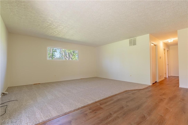 unfurnished room featuring wood finished floors, a textured ceiling, and visible vents