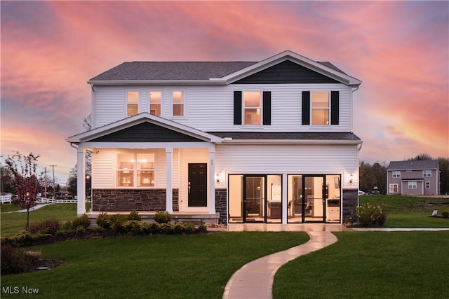 view of front of home with a yard, stone siding, and covered porch