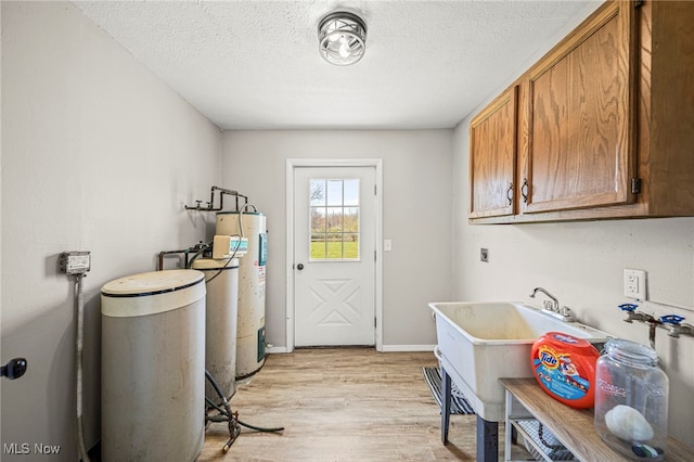 6084 Clay St, Thompson, OH 44086 - laundry area with baseboards, light wood-type flooring, a textured ceiling, electric water heater, and cabinet space