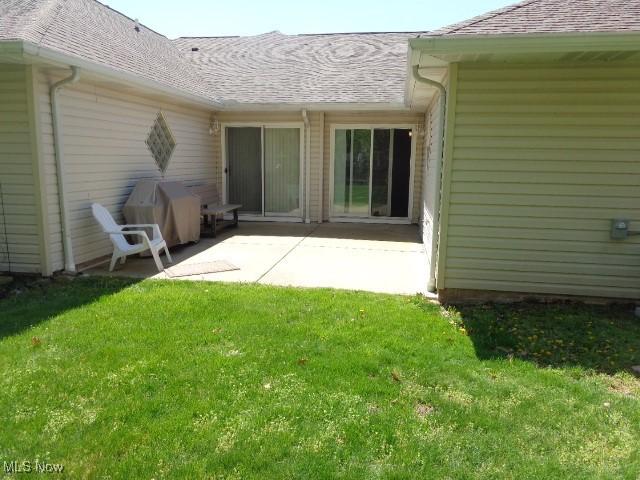 rear view of house with a lawn, a shingled roof, and a patio