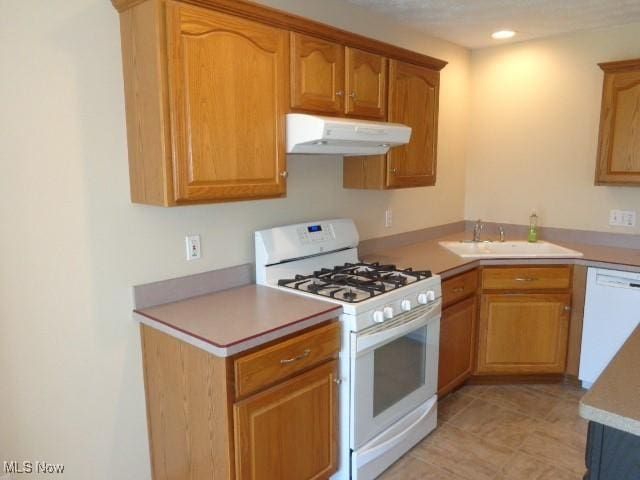 kitchen with a sink, white appliances, light countertops, light tile patterned floors, and under cabinet range hood