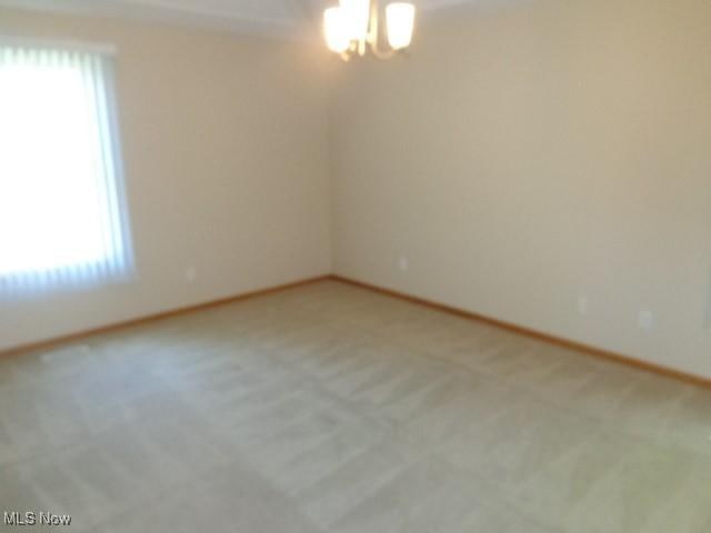 empty room with baseboards, light carpet, a notable chandelier, and a wealth of natural light