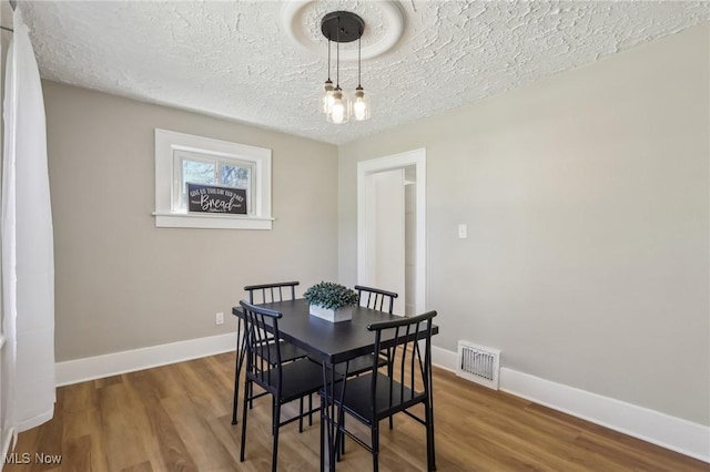 dining room featuring baseboards, a textured ceiling, visible vents, and wood finished floors