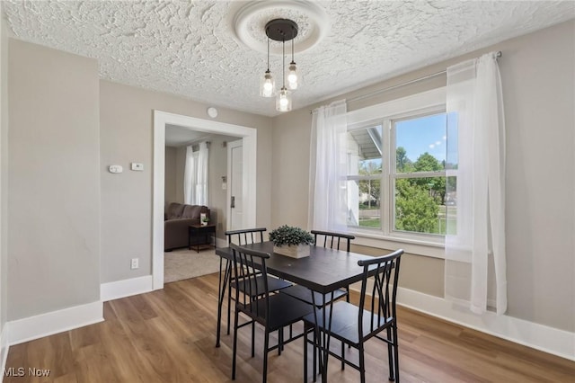 dining area featuring a textured ceiling, baseboards, and wood finished floors