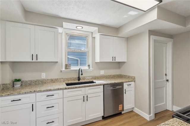 kitchen with white cabinets, a sink, baseboards, light wood-type flooring, and stainless steel dishwasher