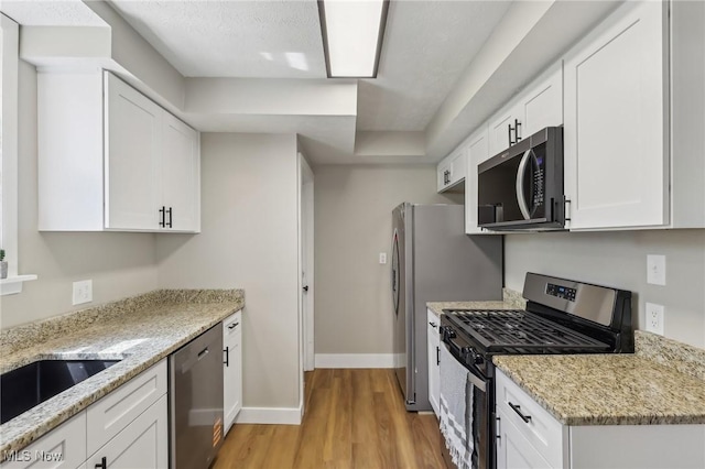 kitchen with white cabinets, baseboards, appliances with stainless steel finishes, and light wood-style floors
