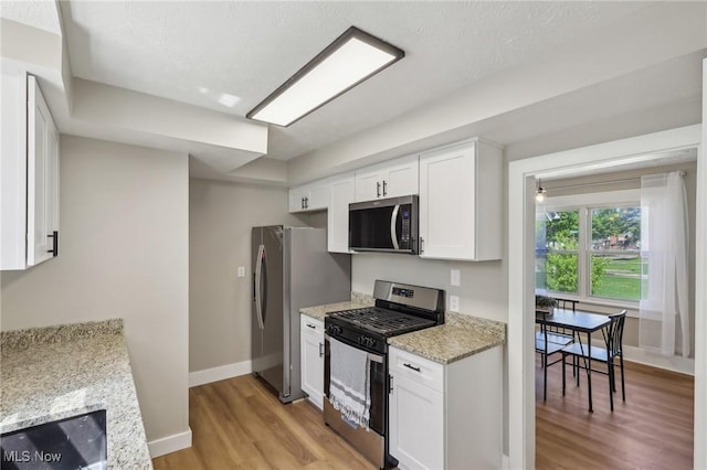 kitchen with light stone countertops, baseboards, white cabinetry, light wood finished floors, and stainless steel appliances