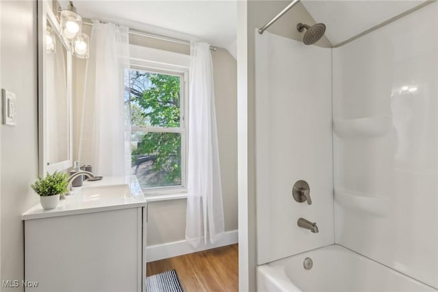 bathroom with baseboards, washtub / shower combination, wood finished floors, and vanity