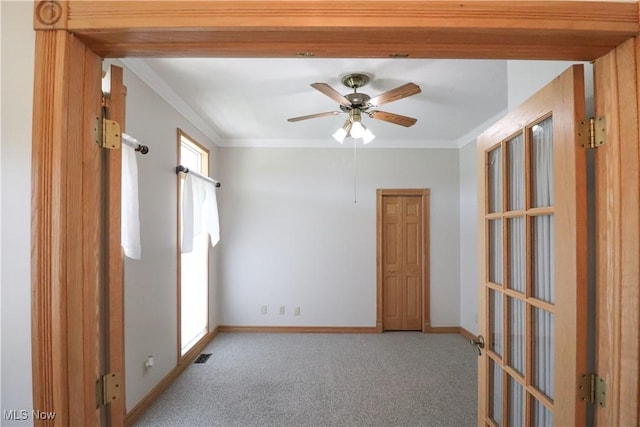carpeted spare room with crown molding, baseboards, ceiling fan, and visible vents