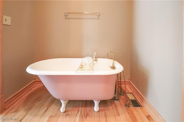 bathroom featuring baseboards, a freestanding tub, wood finished floors, and visible vents