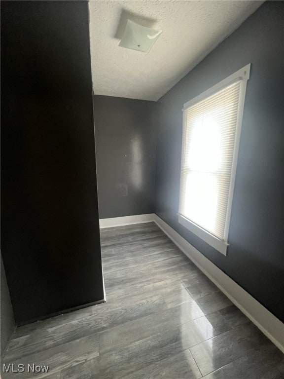 spare room featuring a textured ceiling, baseboards, and wood finished floors