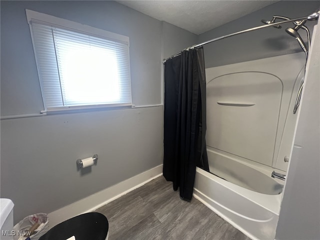 bathroom featuring toilet, a textured ceiling, baseboards, wood finished floors, and shower / tub combo