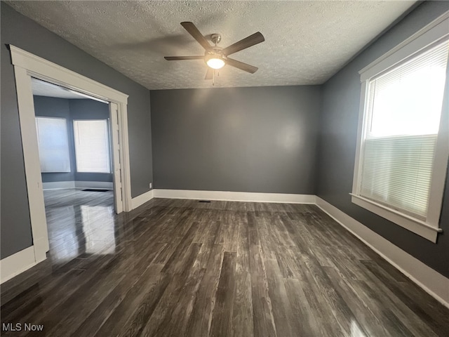 spare room featuring dark wood-type flooring, a textured ceiling, baseboards, and a wealth of natural light