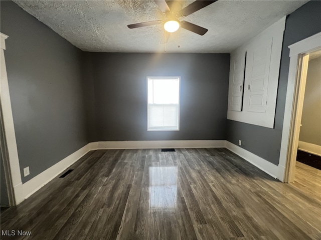 spare room featuring dark wood-style flooring, ceiling fan, a textured ceiling, baseboards, and visible vents