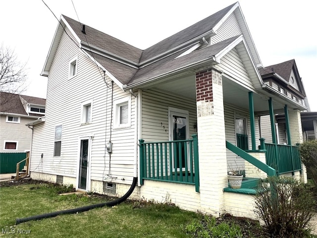 view of side of home featuring roof with shingles, a yard, and a porch
