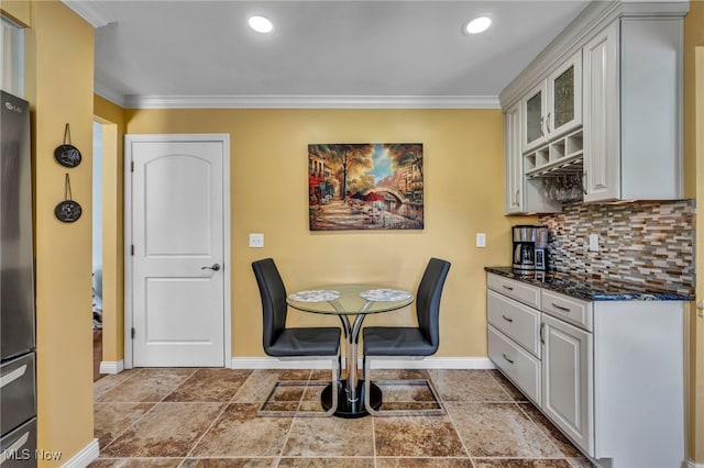 dining room featuring crown molding, baseboards, a bar, stone tile flooring, and recessed lighting
