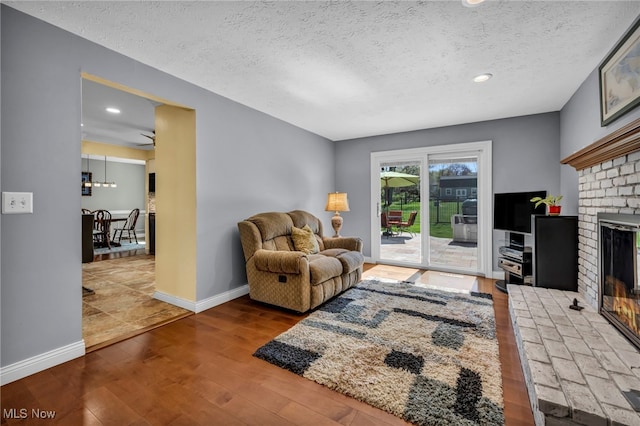 living area featuring baseboards, a textured ceiling, wood finished floors, and a fireplace