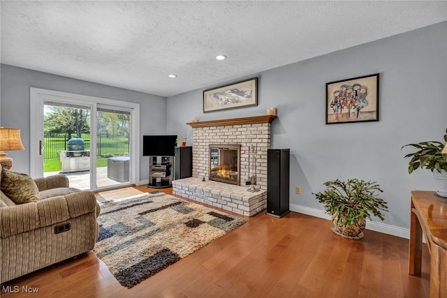 living room featuring a textured ceiling, a fireplace, wood finished floors, baseboards, and recessed lighting
