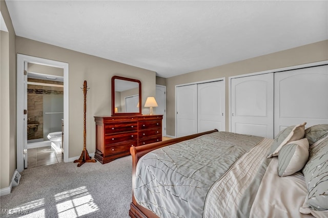 carpeted bedroom featuring baseboards, ensuite bathroom, and two closets