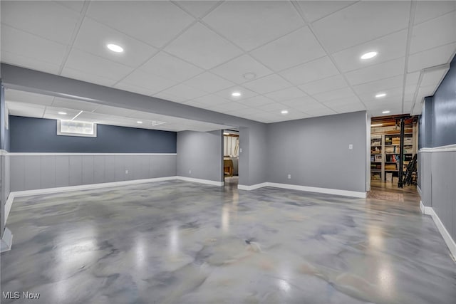 below grade area with baseboards, wainscoting, and a drop ceiling