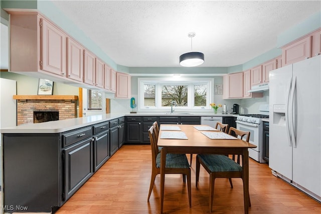 kitchen with light wood finished floors, white appliances, a textured ceiling, a peninsula, and under cabinet range hood