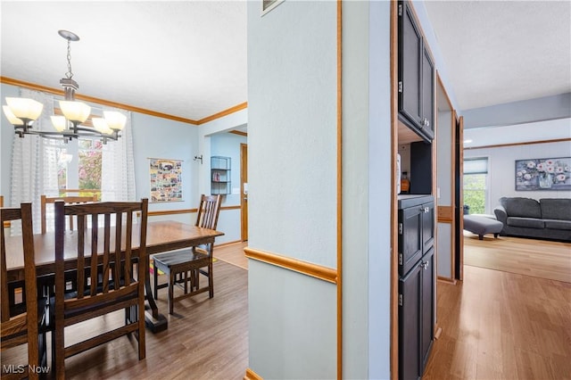 dining area with baseboards, ornamental molding, light wood-type flooring, and a chandelier