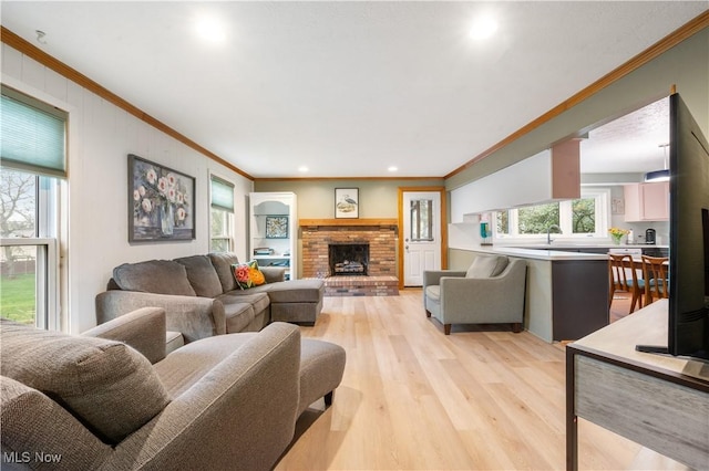 living area with recessed lighting, ornamental molding, a brick fireplace, and light wood finished floors