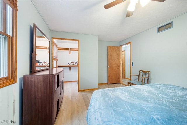bedroom featuring visible vents, light wood-style floors, baseboards, a spacious closet, and a ceiling fan