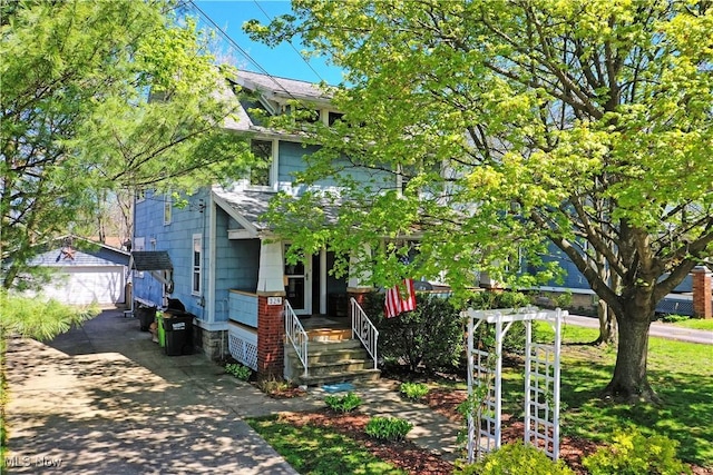 view of front of house featuring a shingled roof, covered porch, and a detached garage