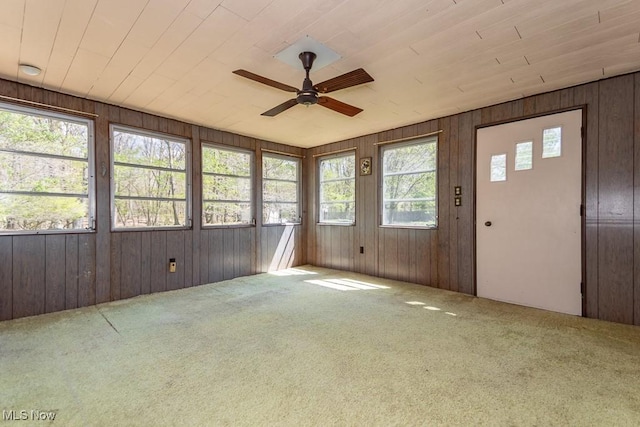 unfurnished sunroom featuring wooden walls, carpet floors, and ceiling fan