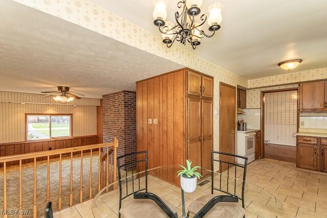 dining room featuring ceiling fan with notable chandelier and wallpapered walls