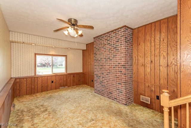 spare room with ceiling fan, carpet floors, a textured ceiling, wood walls, and visible vents