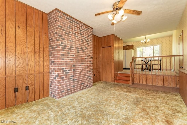 carpeted spare room with ceiling fan with notable chandelier and wood walls